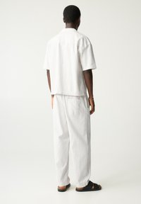 Chemise blanche à manches courtes à rayures, associée à un pantalon ample blanc à rayures. Porté avec des sandales noires, affichant un style décontracté et relax.
