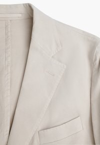 Blazer beige claro hecho de una tela suave, con solapa con muesca, un bolsillo en el pecho y detalles de costura sutiles.