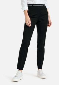 Zwarte slim-fit broek met een gladde textuur, met een middelhoge tailleband, ritszakken en gecombineerd met witte sneakers.