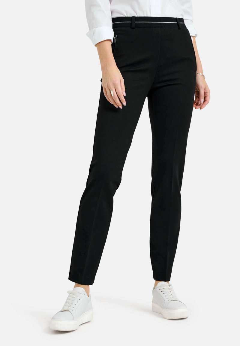 Zwarte slim-fit broek met een gladde textuur, met een middelhoge tailleband, ritszakken en gecombineerd met witte sneakers.