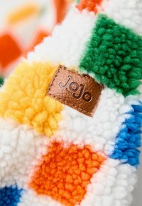 Bunt gemusterte Fleece-Decke mit orangefarbenen, gelben, grünen, blauen und weißen Quadraten, versehen mit einem braunen Lederetikett, das "Jojo" geprägt hat.