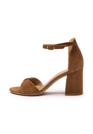 Brązowy zamszowy sandał na wysokim obcasie z zamkniętym tyłem, otwartym noskiem i paskiem wokół kostki. Charakteryzuje się masywnym obcasem i gładką podszewką wewnętrzną.