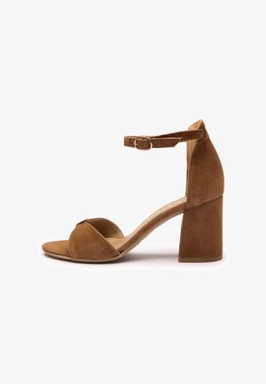 Brązowy zamszowy sandał na wysokim obcasie z zamkniętym tyłem, otwartym noskiem i paskiem wokół kostki. Charakteryzuje się masywnym obcasem i gładką podszewką wewnętrzną.