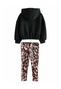 Haut cropped noir avec capuche et manches larges, associé à des leggings roses ornés d'un motif léopard noir.
