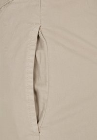 Pantalons en coton beige avec une poche latérale et des coutures visibles. Le tissu a une finition lisse et légèrement texturée.