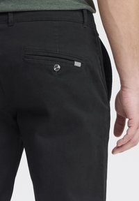 Czarne spodnie o gładkiej fakturze, z tylną kieszenią zapinaną na guzik oraz paskowanym akcentem na krawędzi.