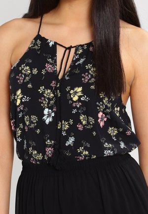 Vrouw draagt een zwarte haltertop met een meerkleurige bloemenprint en verstelbare strikceintuur, gecombineerd met een zwarte rok met hoge taille.