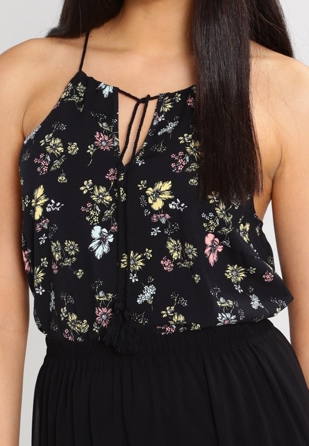 Femme portant un haut noir à col halter avec un imprimé floral multicolore et un col ajustable à nouer, associé à une jupe noire taille haute.