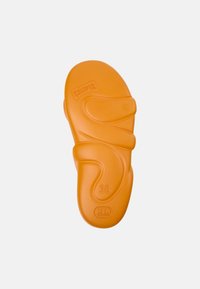 Oranssi kumi-sandaali, jossa on aaltoileva pohjasuunnittelu. Pohjassa on kohokuvioitu "CAMPER"-logo ja koko "38". Pinta on sileä.