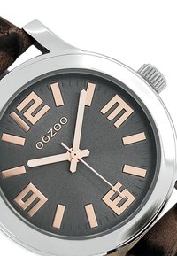 Montre analogique ronde avec un cadran gris foncé, des marqueurs d'heure en or rose et un bracelet en cuir marron. Boîtier en acier inoxydable avec une finition polie.