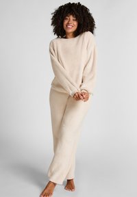 Beige fleece lounge-outfit set met een langemouwen top en bijpassende broek, zachte textuur, relaxte pasvorm en geribbelde boorden bij de polsen en enkels.