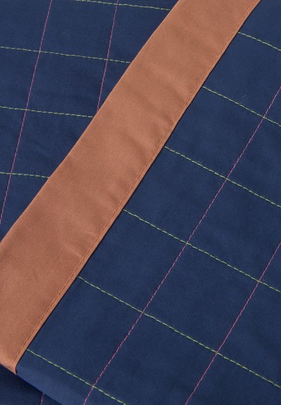 Gros plan d'un tissu matelassé bleu marine avec des coutures croisées roses et jaunes et une bande diagonale en tissu marron.