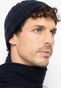 Gebreide marineblauwe muts en sjaal set; zachte textuur met ribbelpatroon; ronde vorm van de muts, wikkelontwerp van de sjaal zichtbaar.