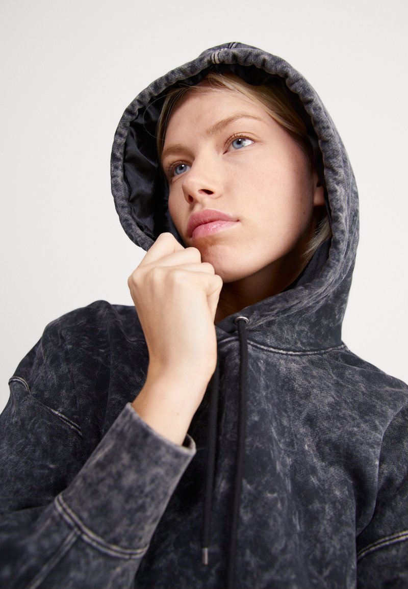 Sudadera negra con un diseño texturizado y desgastado. Presenta una gran capucha, cordones y detalles de costura visibles en las mangas y el dobladillo.