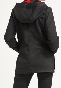 Giacca in pile nera con cappuccio, caratterizzata da una fodera a quadri. Tessuto liscio e vestibilità sagomata, con dettagli di cucitura e tasche laterali.