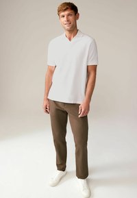 Biała koszulka polo z krótkim rękawem w połączeniu z brązowymi spodniami slim-fit i białymi sneakersami. Ubranie posiada klasyczny kołnierzyk i gładkie tekstury.