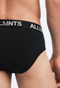 Black cotton briefs featuring a wide elastic waistband with "ALLSAINTS" logo. Close-fitting design with smooth texture and minimal stitching.