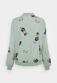 Hellgrüne Bomberjacke mit floralen Mustern in Marineblau, Weiß und Braun, Rippstrickbündchen und Kragen sowie einem gerafften Saum.