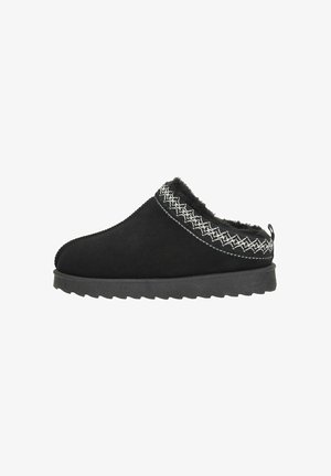 Chausson noir à enfiler avec semelle épaisse, doublure en fourrure douce et motif brodé blanc autour de l'ouverture.