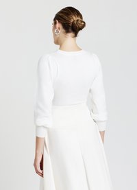 Weißer Strickpullover mit puffartigen langen Ärmeln, gerippten Bündchen und rundem Ausschnitt, kombiniert mit einem weißen Rock, von hinten betrachtet.