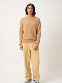Hellbrauner Kaschmirpullover mit Rundhalsausschnitt, kombiniert mit lockeren gelben Hosen und schwarz-weißen Turnschuhen. Minimalistisches Design, glatte Textur.