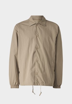 Jachetă bej deschisă, fabricată dintr-un material texturat, cu închidere prin nasturi, guler, manșete elastice și tiv cu șnur reglabil.