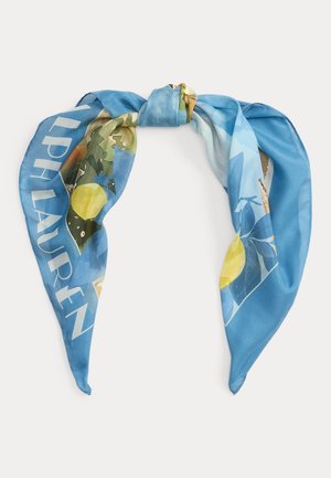 Pañuelo de seda azul con estampados de limones y hojas, anudado en el centro, con texto grande blanco parcialmente visible en el borde.