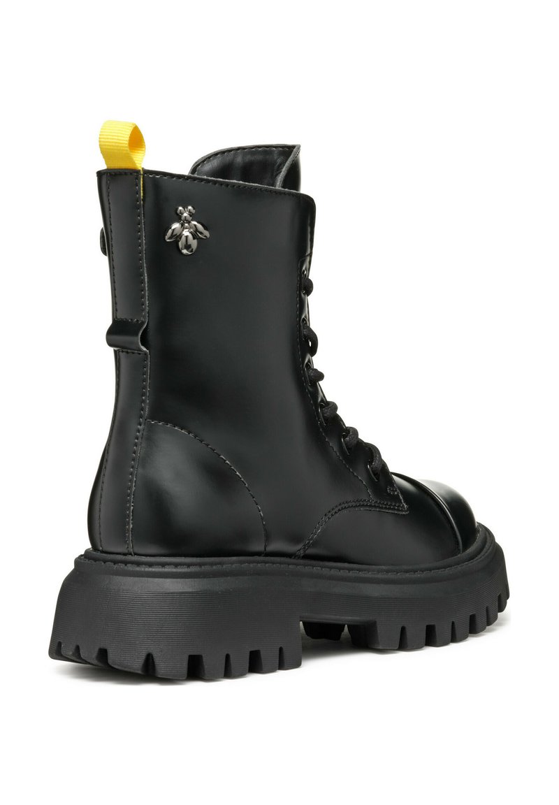 Stivale alla caviglia in pelle nera con suola nera spessa, design con lacci e un'etichetta gialla. Presenta un dettaglio decorativo a forma di ape argentata sul lato.