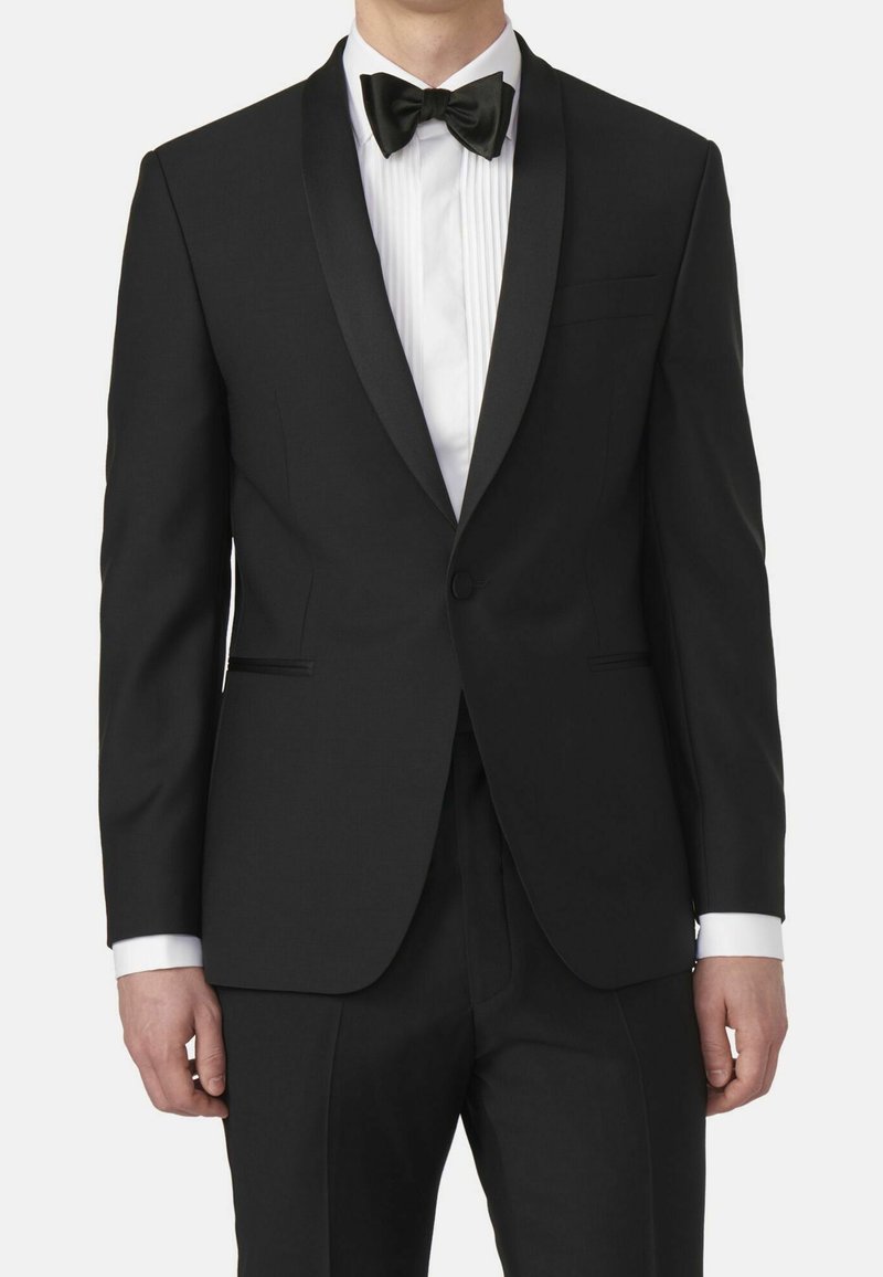 Zwarte tuxedo met satijnen revers, witte geplooide shirt en zwarte vlinderdas. Stof lijkt glad met een op maat gemaakte pasvorm. Klassiek formeel ontwerp.