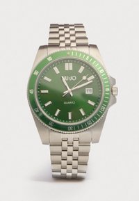 Vihreä kvartsikello, jossa on ruostumattomasta teräksestä valmistettu ranneke, pyöreä kuori, heijastavat merkit ja päivämääränäyttö kello kolmessa. 60 minuutin bezel samansävyisessä vihreässä.