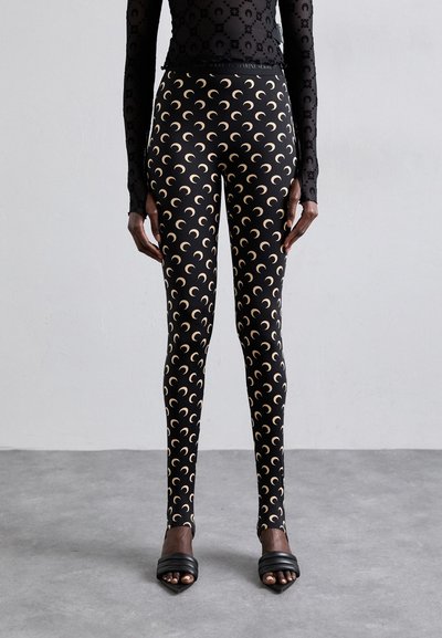 Leggings neri con un motivo di lune crescenti ripetuto in un leggero color beige. Tessuto liscio e elasticizzato con un design aderente.