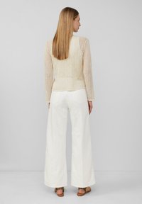 Hellbeige gestrickter Pullover mit gestreiftem Muster, kombiniert mit weißen weit geschnittenen Hosen. Sandalen mit Tiermusterakzenten runden das Outfit ab.