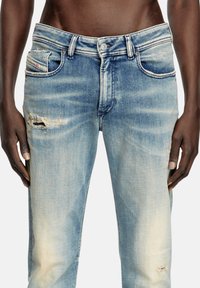 Bledi modri kavbojki z obrabljenim dizajnom, ki imajo svetlejše poudarke, pet žepov in zapiranje na gumb.