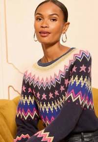 Granatowy sweter z dzianiny z geometrycznymi i gwiaździstymi wzorami w odcieniach różu, złota i niebieskiego. Żebrowany dekolt i mankiety, miękka tekstura.