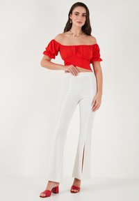 Rød off-shoulder top med flæser, parret med hvide flared bukser med sideslids og lodrette striber. Røde open-toe hæle.