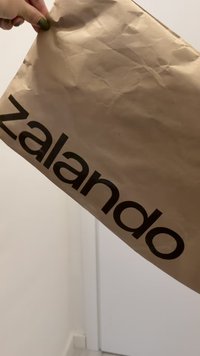 Busta di carta marrone con una texture stropicciata, con la scritta "zalando" in nero e in grassetto sul davanti, tenuta contro uno sfondo semplice.