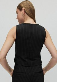 Svart rutig väst med rak halsringning och skräddarsydd passform. Har en kortad längd och diskreta kantdetaljer.