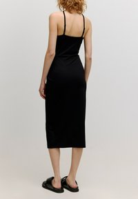 Zwarte jurk met dunne bandjes, aansluitend ontwerp, knielengte, gladde textuur, gecombineerd met zwarte schuifsandalen. Eenvoudige en strakke uitstraling.