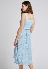 Débardeur bleu clair avec des bords festonnés, associé à une jupe fleurie bleue, dotée d'une taille élastique et d'une coupe mi-longue.