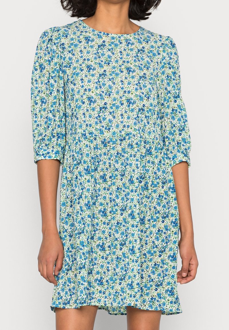 Robe à fleurs avec des motifs bleus et verts sur un fond clair. Dotée d'un col rond et de manches bouffantes trois-quarts. Tissu texturé.