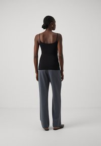 Black spaghetti strap top paired with gray wide-leg trousers. Smooth fabric with a fitted silhouette and subtle sheen. Simple design.