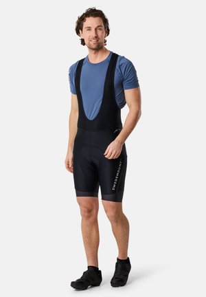 Pantaloni da ciclismo neri con taglio ergonomico, spalline in rete e inserto imbottito; abbinati a una maglia a maniche corte blu e scarpe da ciclismo nere.