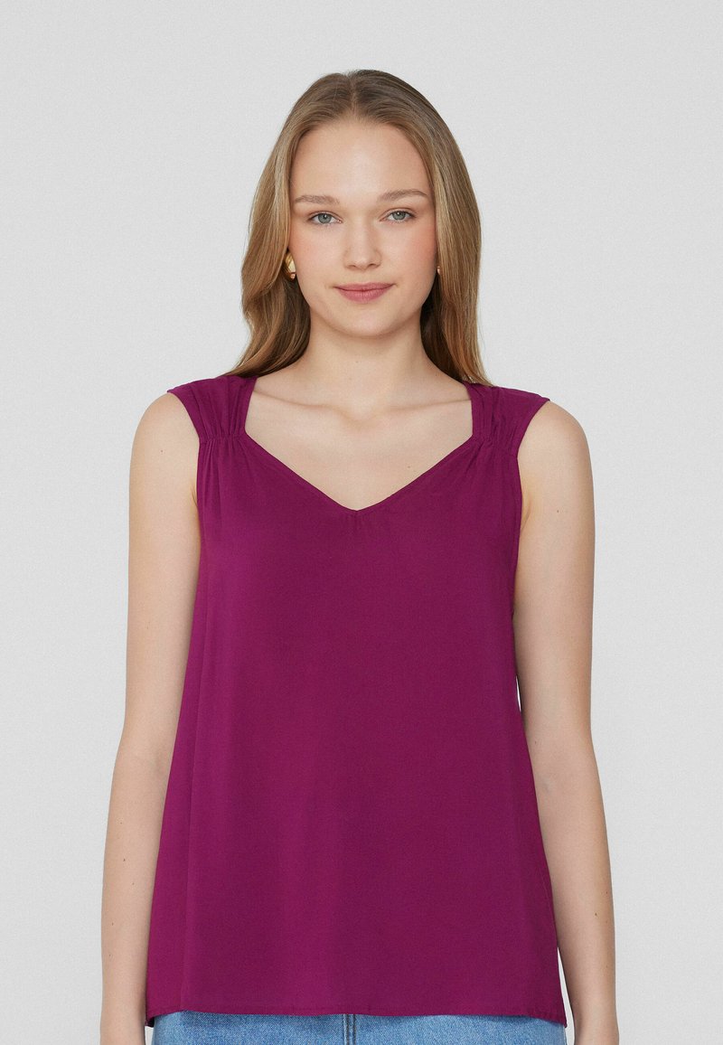 Top sin mangas de color violeta con escote en V, detalles de hombros fruncidos y tela suave. Diseño simple sin patrones ni adornos.