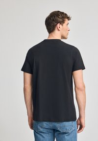 T-shirt nera a maniche corte in cotone, con collo rotondo e vestibilità rilassata; design semplice senza motivi o dettagli.