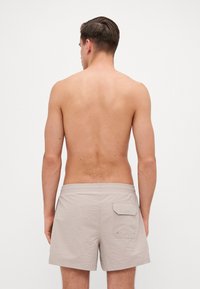 Shorts de bain beige avec une finition texturée, taille élastique et une poche arrière unique, présentés de dos sur un fond uni.