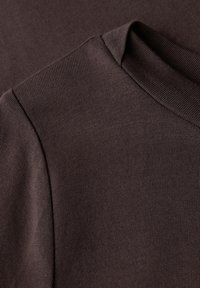 Gros plan sur un tissu en maille marron montrant la couture et le col côtelé d'un vêtement, mettant en avant la texture et les détails de la couture.