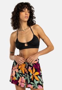Haut de bikini noir avec tissu froncé et détail en trou de clé ; associé à un short à motifs floraux vibrants en rose, orange et vert.
