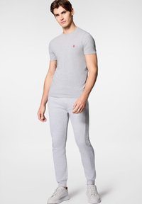 Szary dopasowany t-shirt i pasujące dresy, wykonane z miękkiego materiału, z małym czerwonym logo na klatce piersiowej i prążkowanymi mankietami przy kostkach.