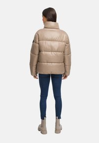 Beige puffjacka med hög krage, med en quiltad design, bärs över blå jeans och beiga ankelboots.