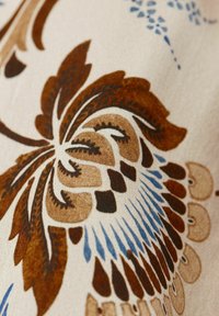 Textil mit floralem Design in Brauntönen, Blau und Creme. Auffällige Details sind komplizierte Muster und eine sanfte Textur.